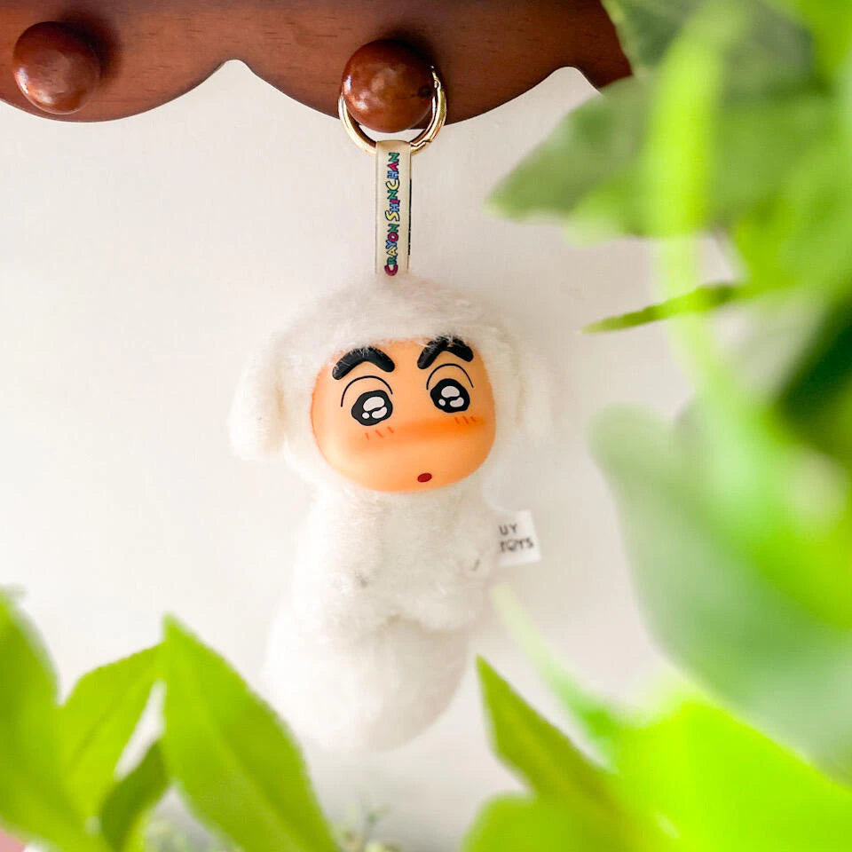 White dog-costume Shinchan Big Tails plush keychain held among green leaves
