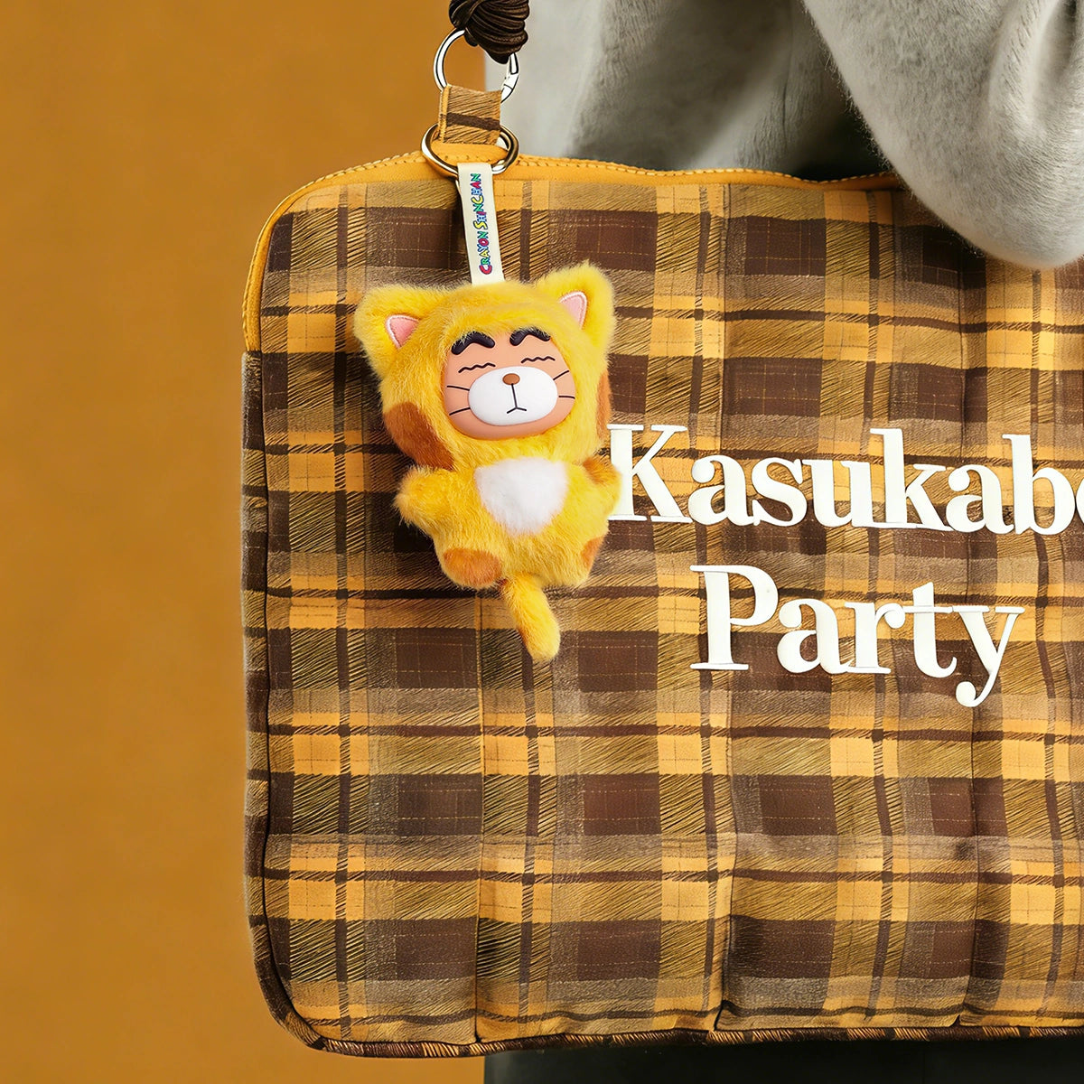 Leopard Shinchan plush charm in yellow cat onesie clipped to a plaid Kasukabe Party bag, Crayon Shinchan