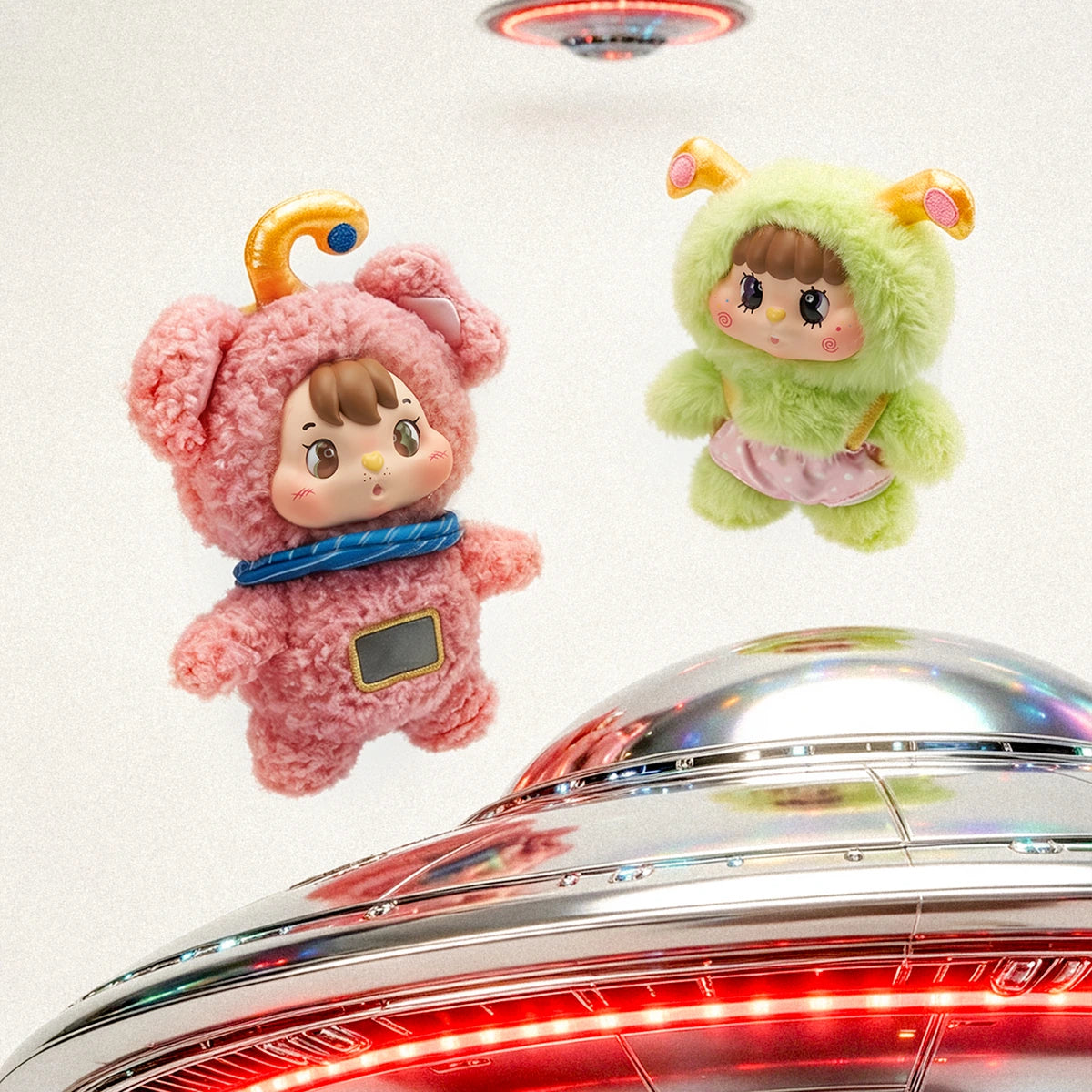 Pink bear and green alien-cat Little Buns plush characters hovering above a UFO prop