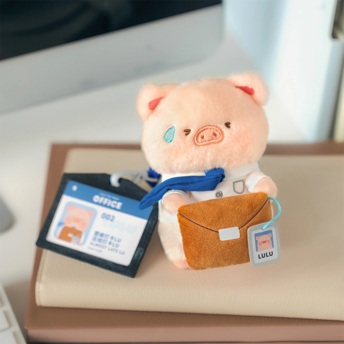 Almost Late Lu piggy plush keychain with sweat drop and briefcase on a desk, LuLu Piggy Office