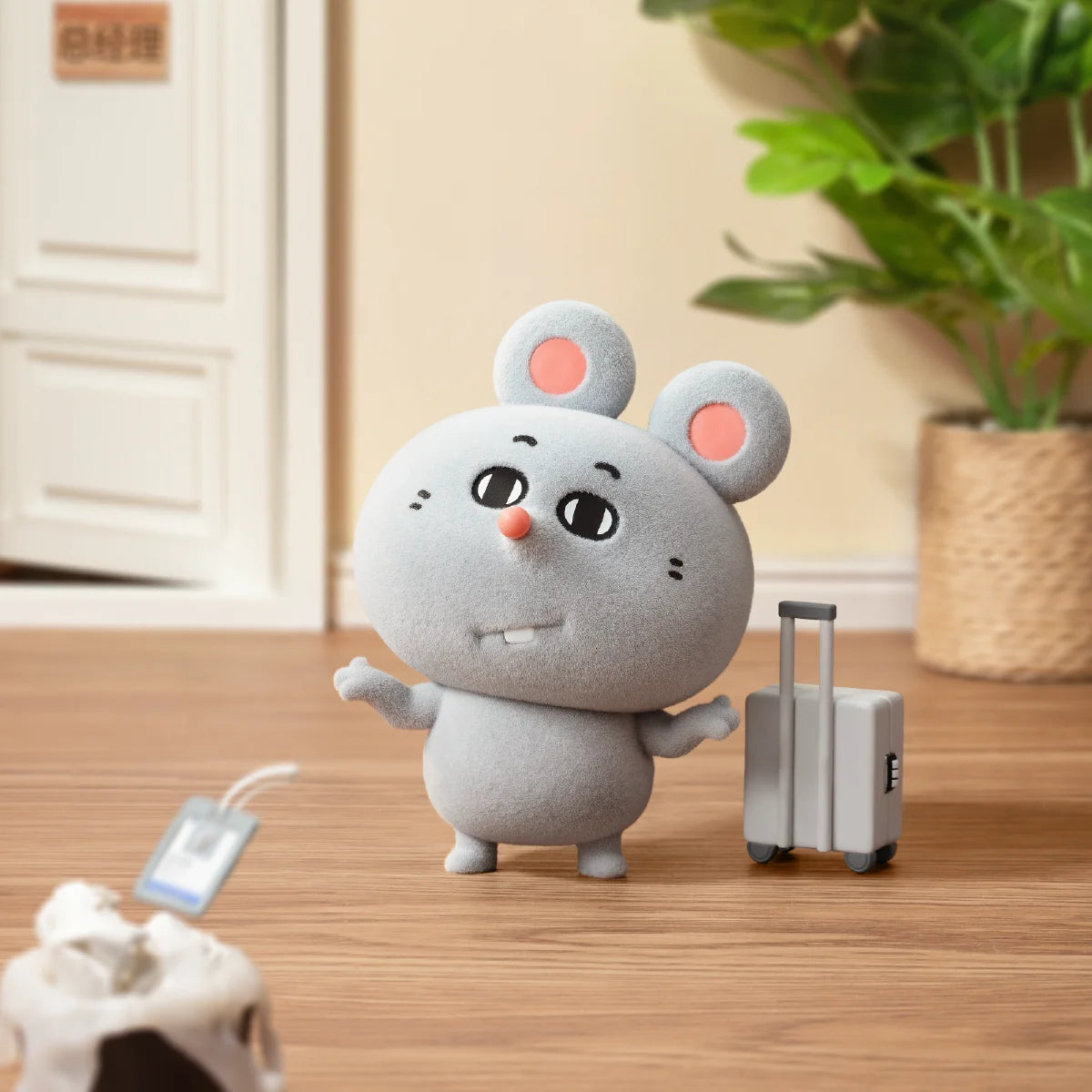 Meiji corporate mouse standing beside a silver rolling suitcase at home