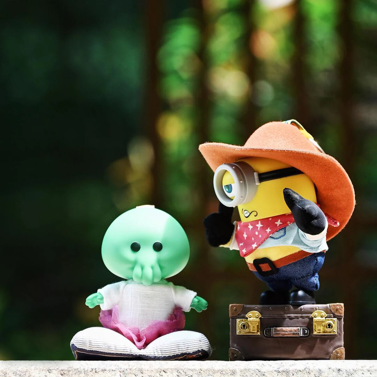 Goomi and Cowboy James plush toys posed in a forest with a suitcase