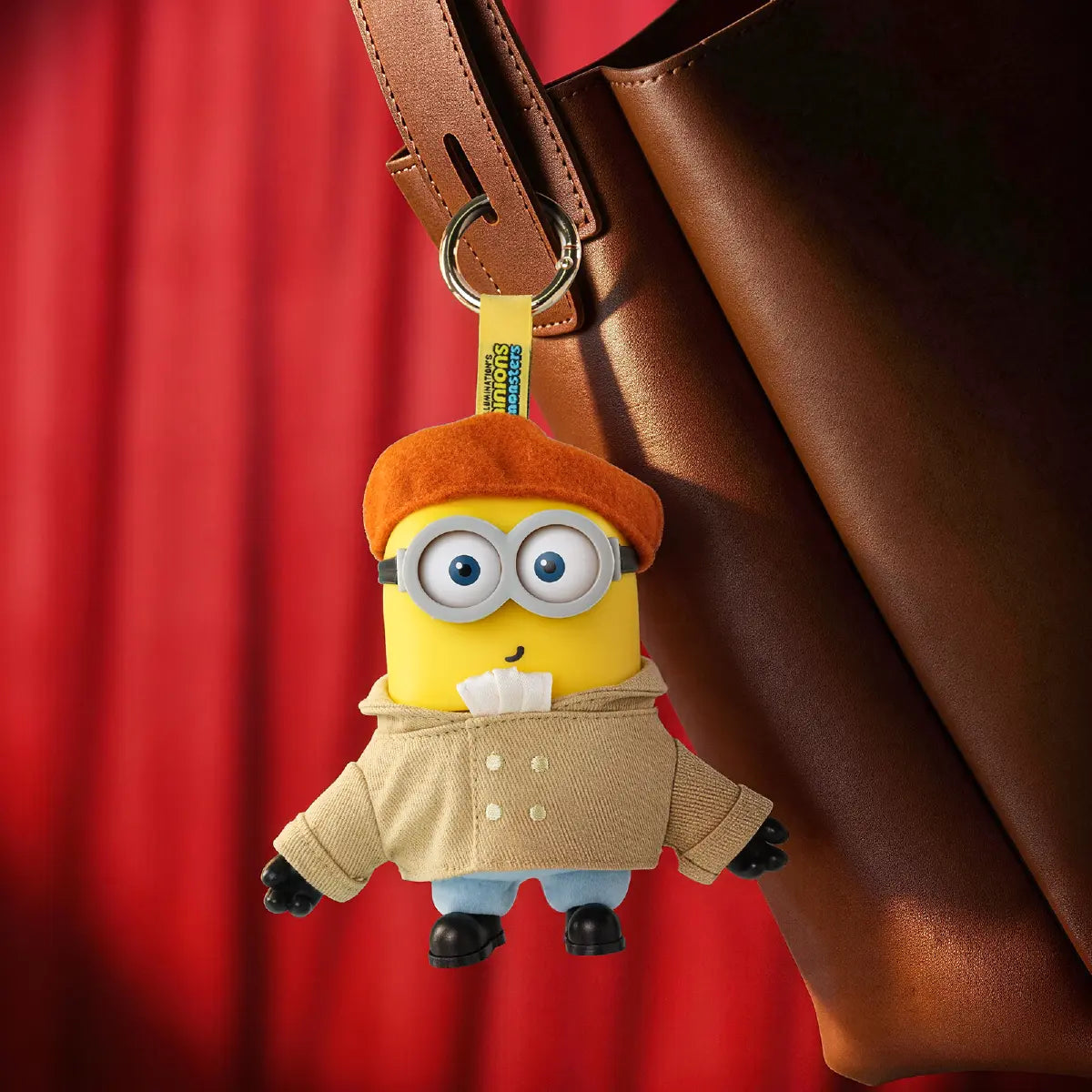 Artist Henry Minion plush keychain hanging from a brown leather bag