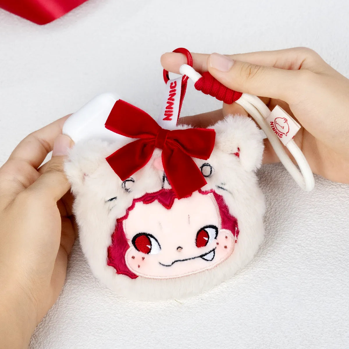 Hands holding the NINNIC Party Kitty plush charm with red bow and tag, Wild & Free scented charm