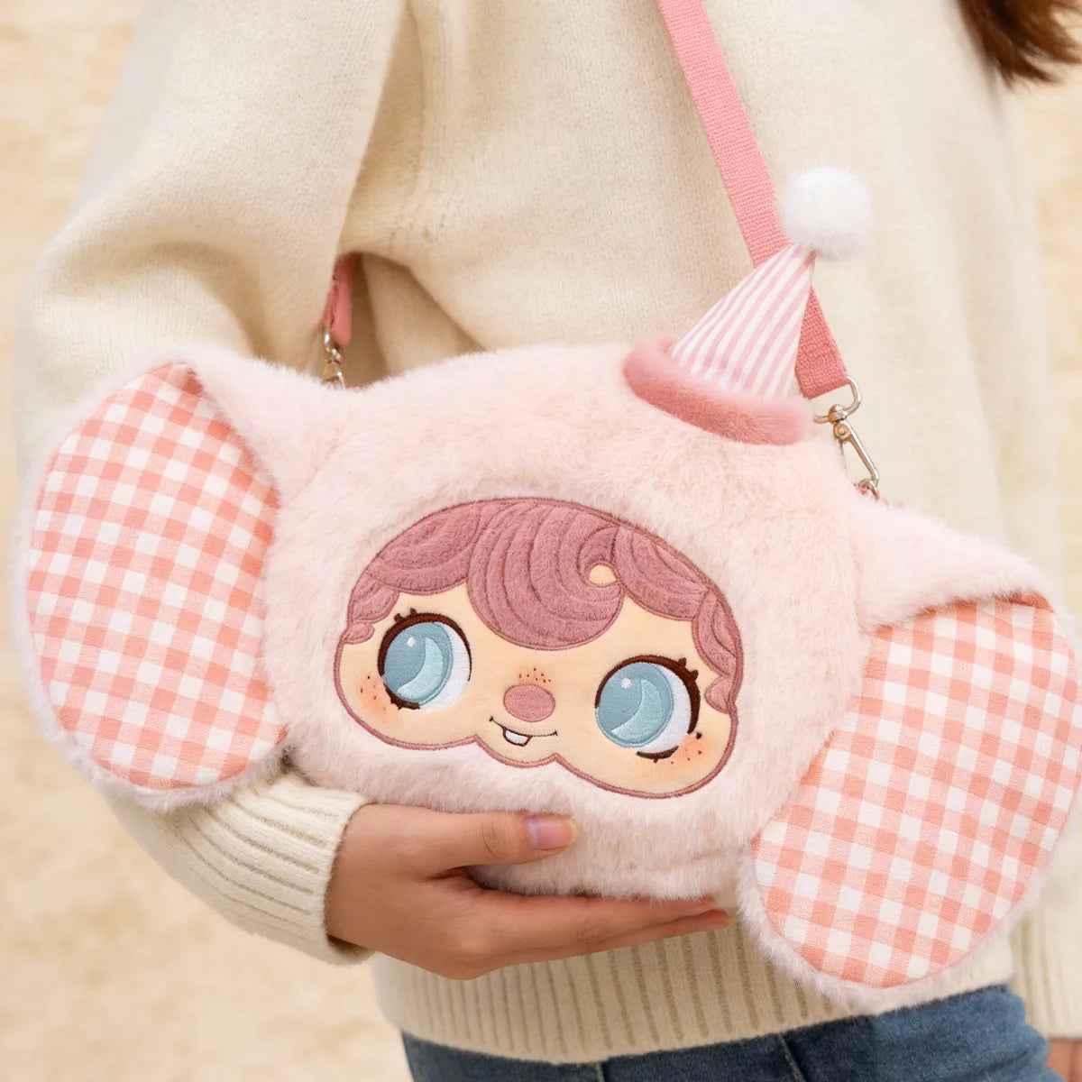 Model holding the pink Pouka Magic Elephant plush bag with checkered ears and freckled face, POUKAPOUKA