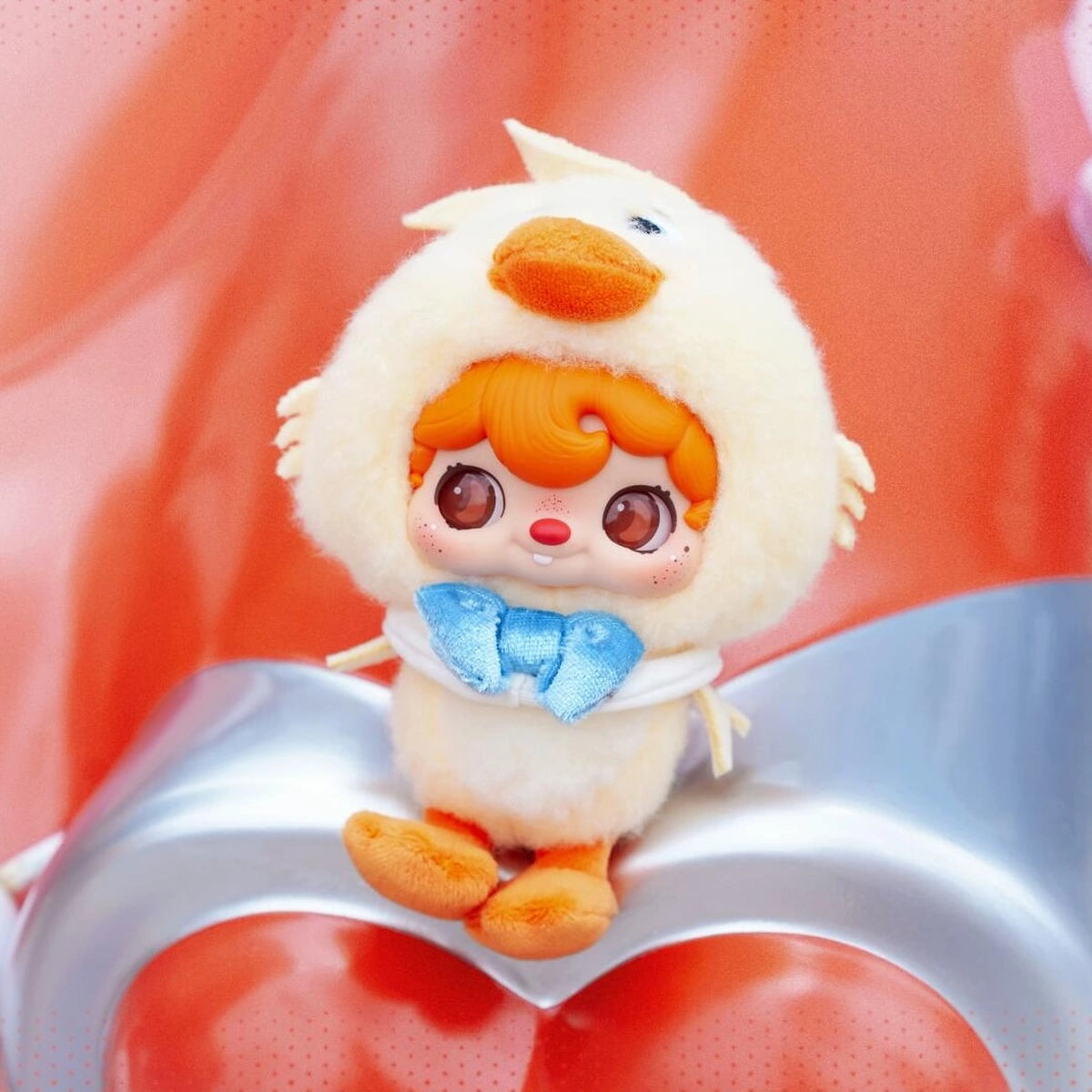 POUKAPOUKA in a Quacker duck costume seated on a silver heart cushion
