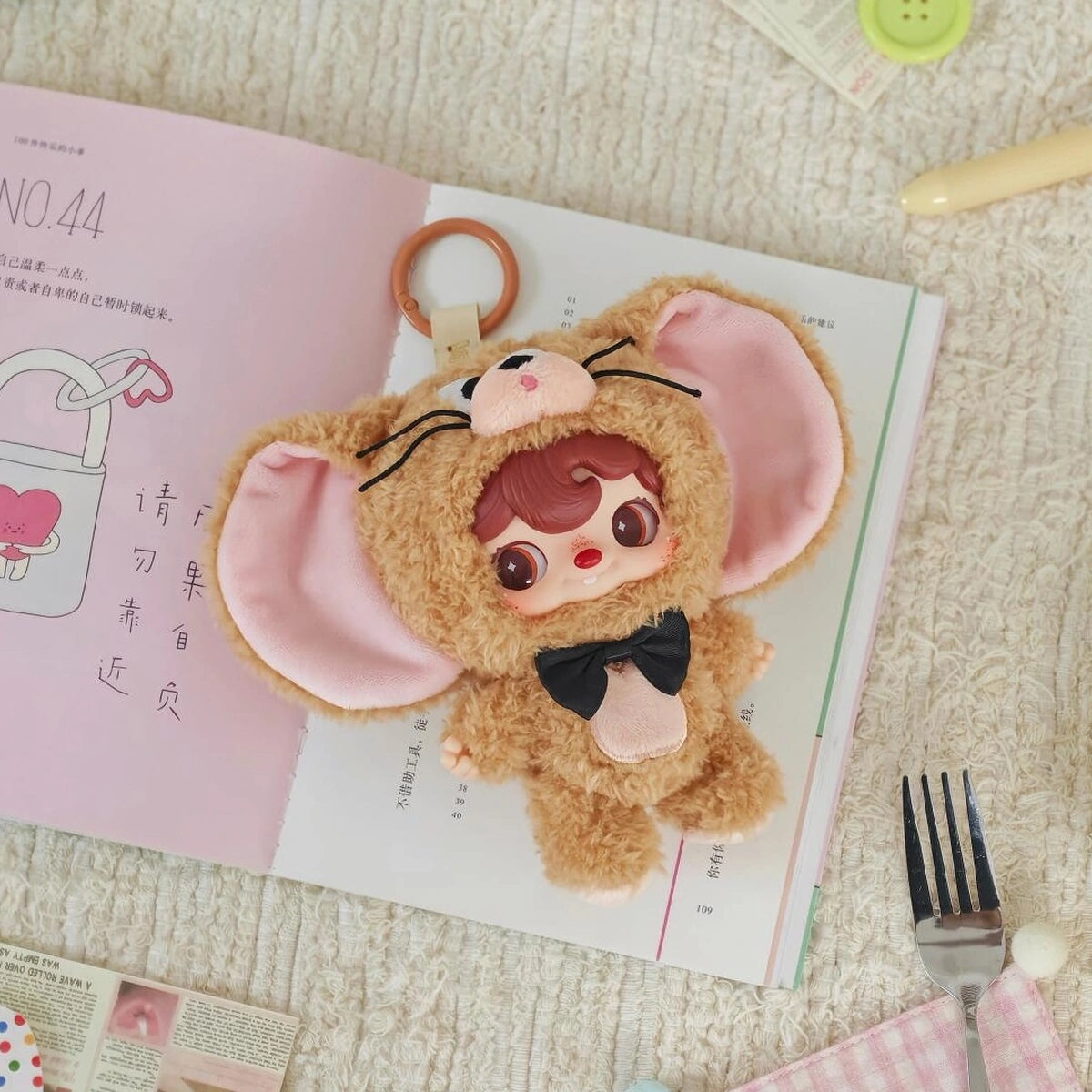 POUKAPOUKA brown Jerry costume plush keychain lying on an open book