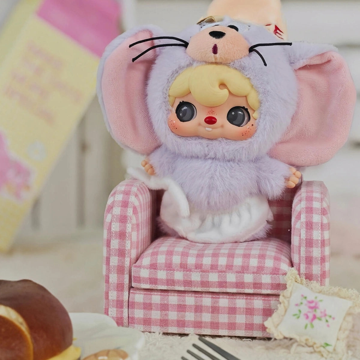 POUKAPOUKA in a gray Tom costume seated in a miniature pink armchair