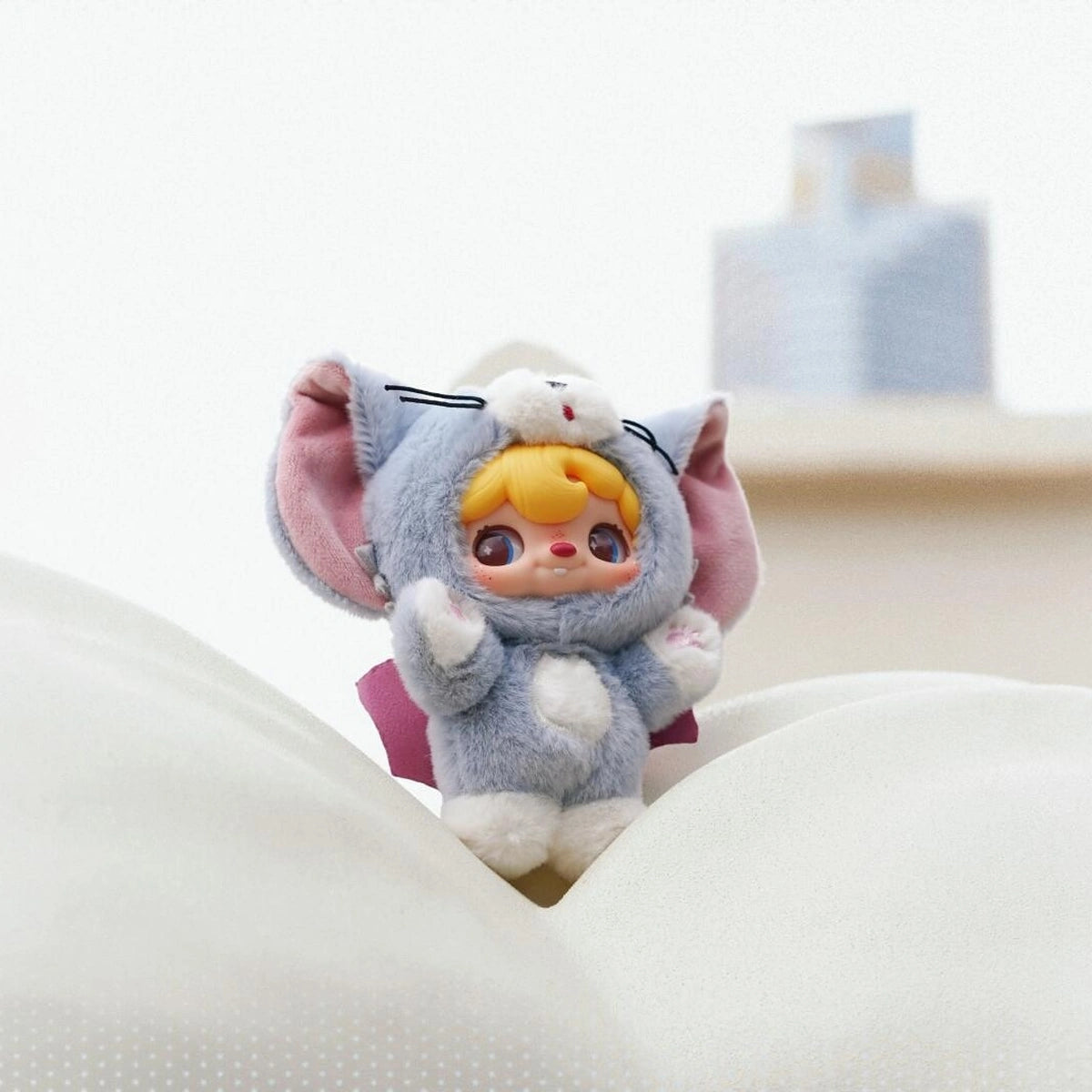 POUKAPOUKA in a gray Tom costume standing among white cushions
