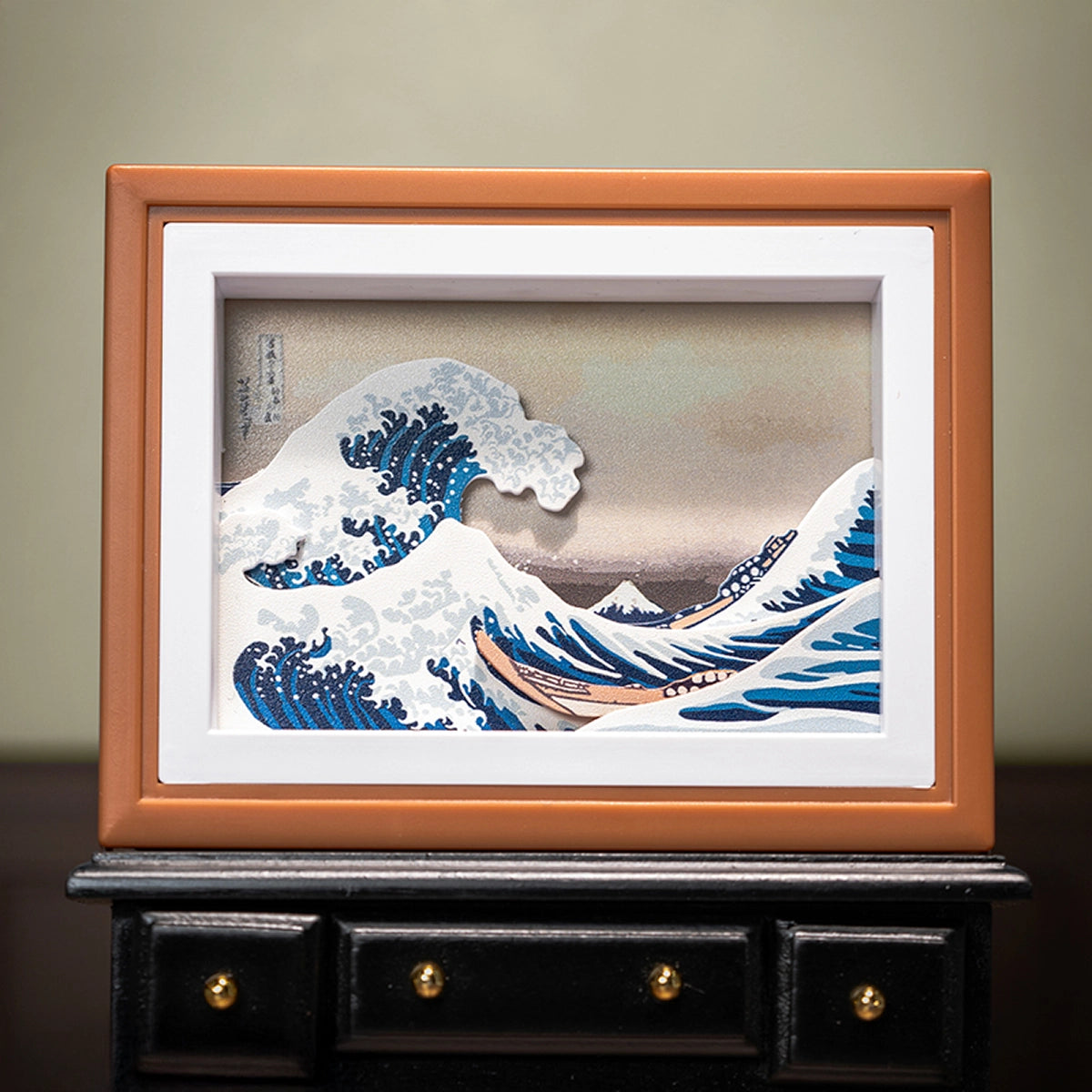 The Great Wave off Kanagawa paper-cut diorama in orange frame on a black table, QueSera Living Paintings