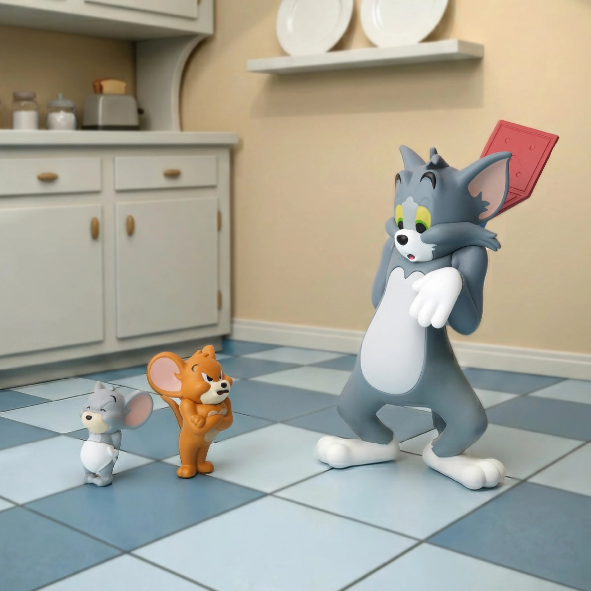 Tom holding a red flyswatter as Jerry and Tuffy confront him in a kitchen