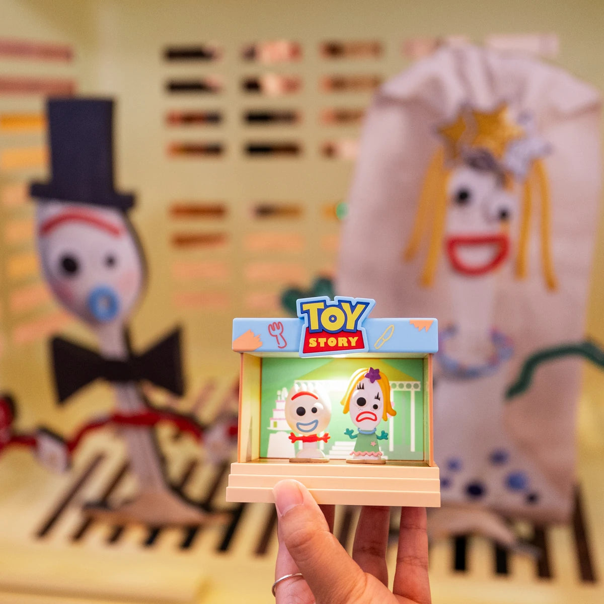 Hand holding the Forky and Karen Beverly stage figure in front of matching artwork
