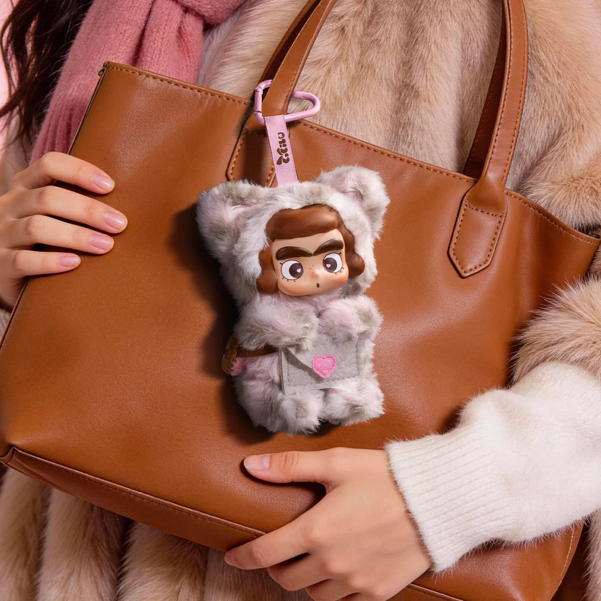 CiCiLu Rosé leopard messenger plush keychain hanging from a tan tote bag