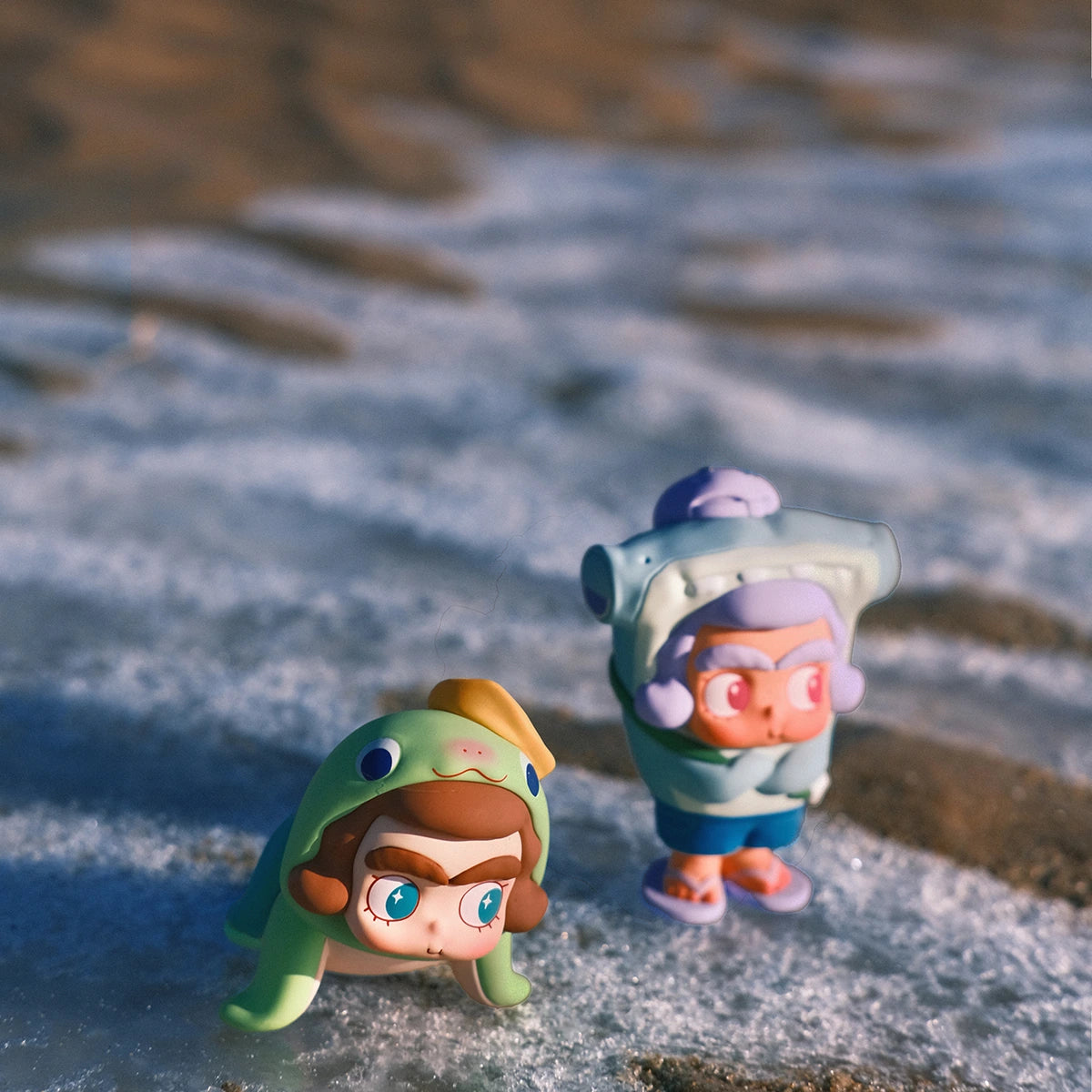 CiCiLu figures in green fish and blue sea-animal hoods standing on the wet shoreline