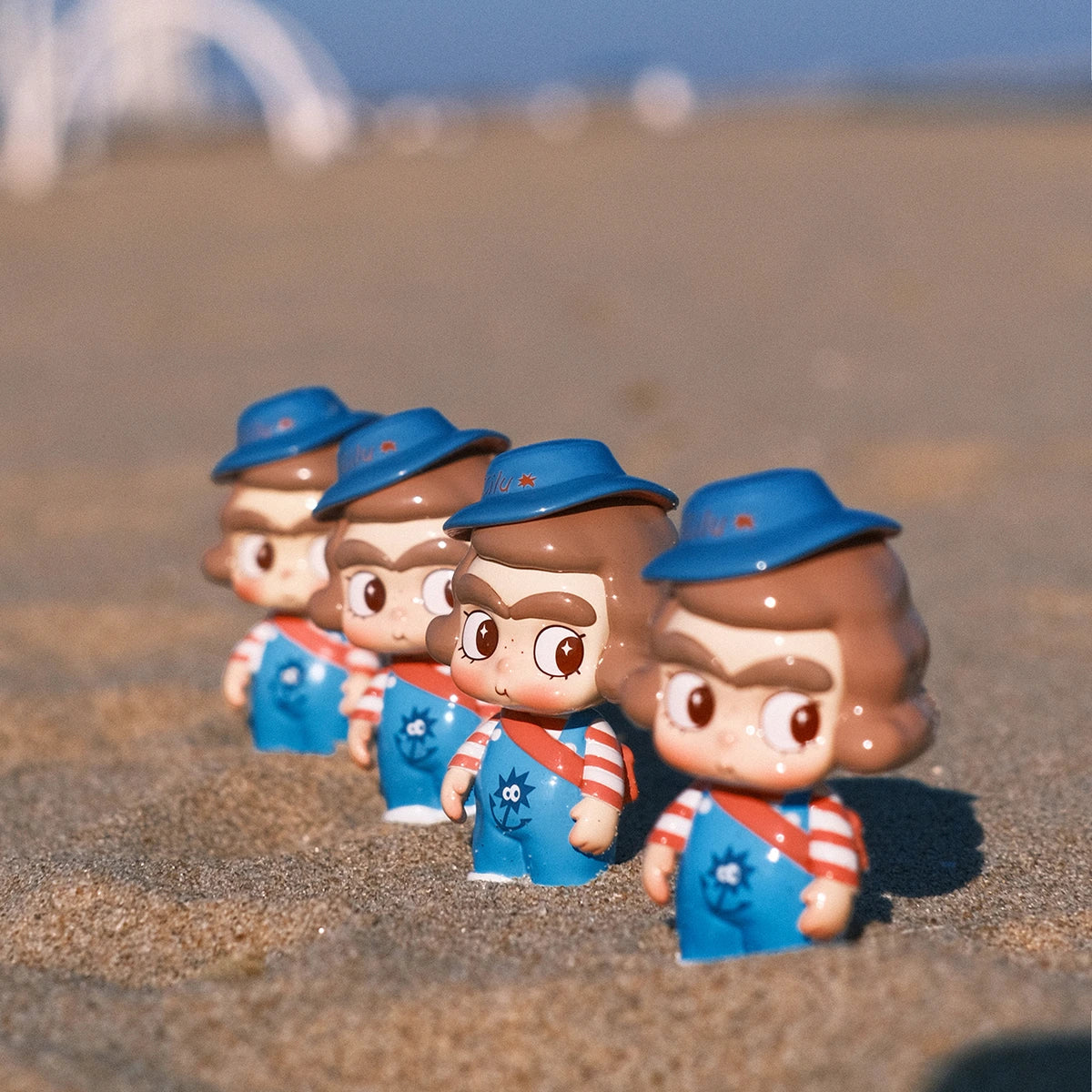 Four CiCiLu sailor figures in blue hats, striped shirts, and overalls lined up on the sand