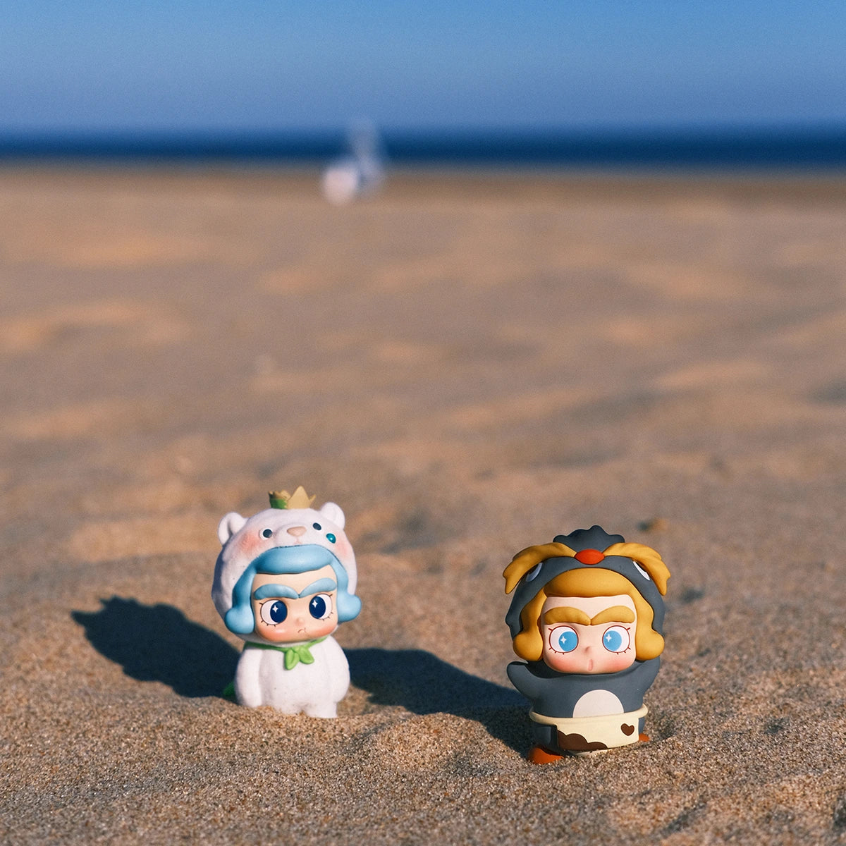 CiCiLu figures in white sea-animal and black penguin costumes half-buried in beach sand