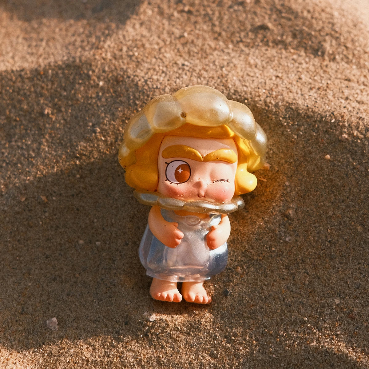 Winking blonde CiCiLu in a translucent jellyfish-inspired dress standing on the beach