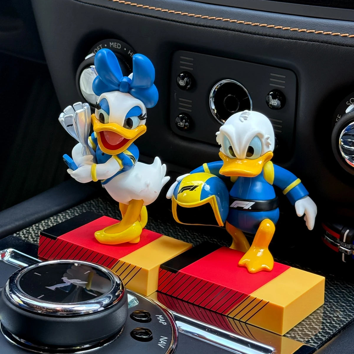 Daisy Duck trophy and Donald Duck helmet figures displayed in a car console