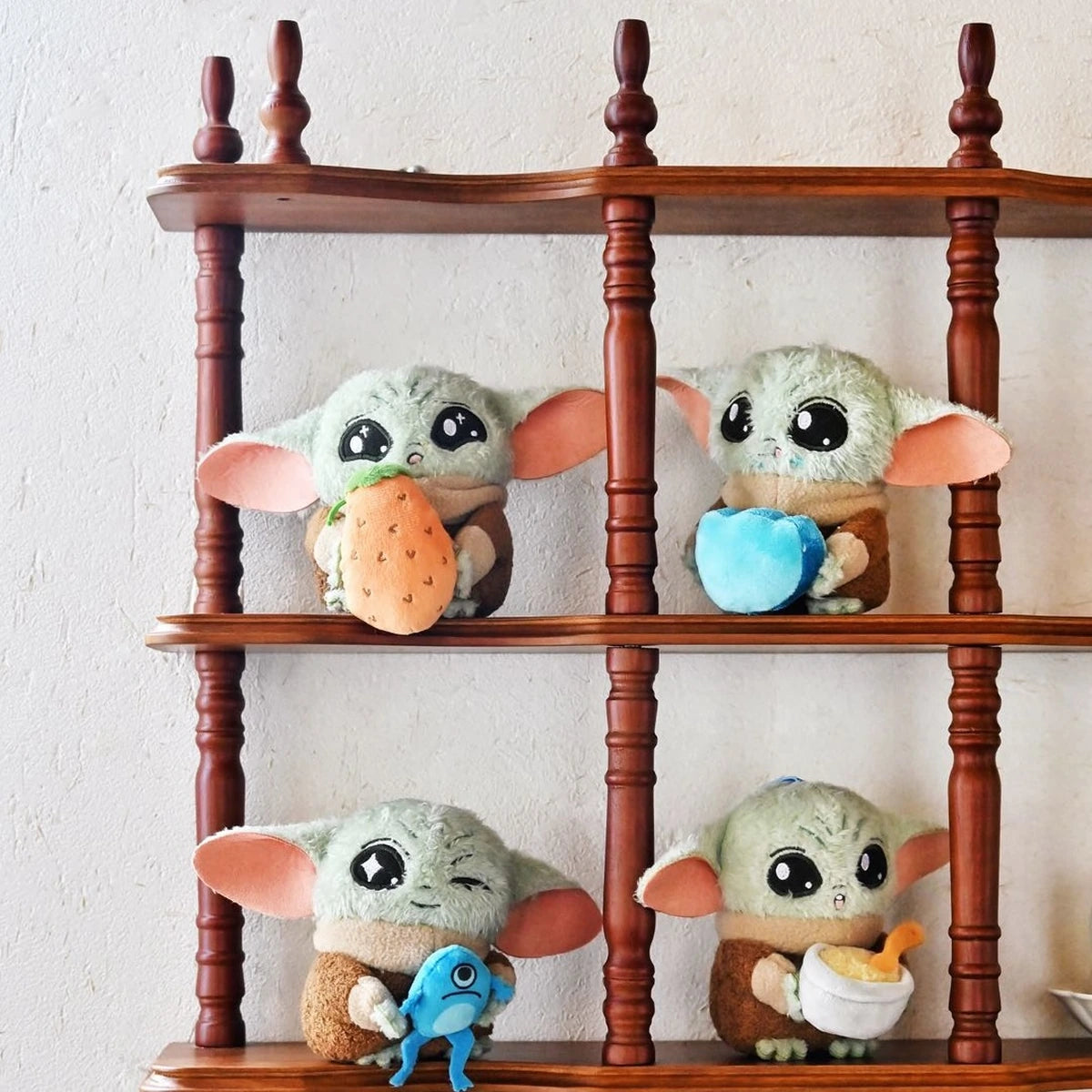 Four Grogu plush designs displayed in the compartments of a wooden shelf