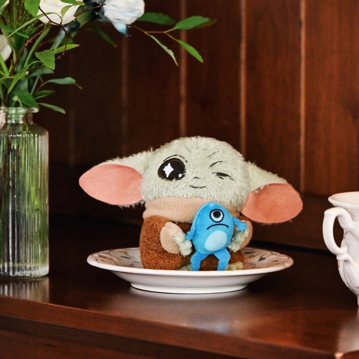 Winking Grogu plush holding a blue frog creature on a white saucer
