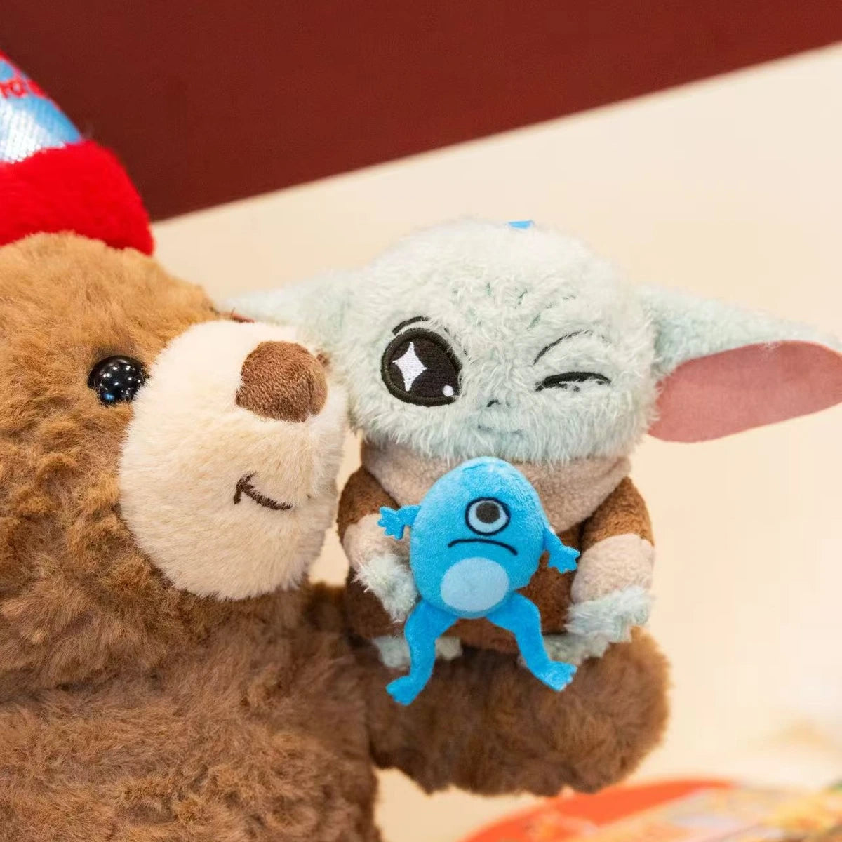 Winking Grogu plush with blue frog creature leaning against a brown teddy bear