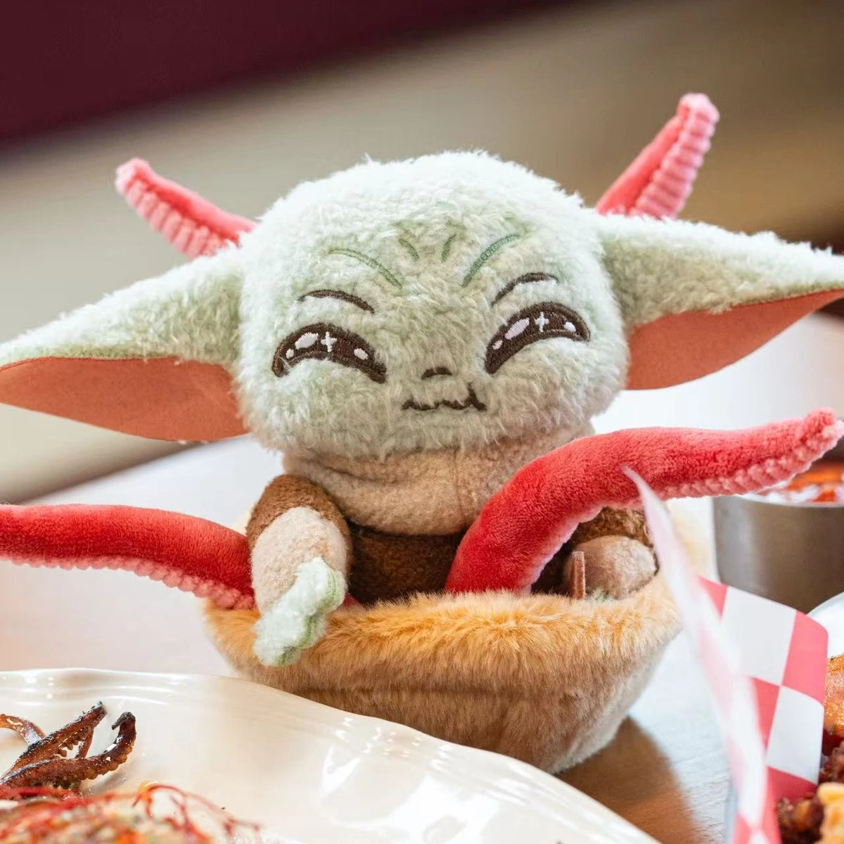 Close view of smiling Grogu plush in a basket with red tentacles at a restaurant table
