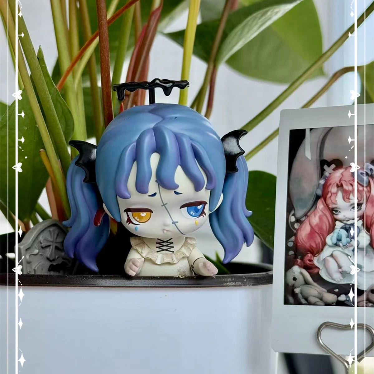 Blue-haired horned Lilith peeking from a white plant pot beside a photo card