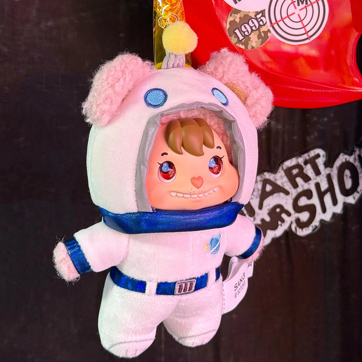 Little Buns white bear astronaut plush keychain hanging in front of a graphic T-shirt