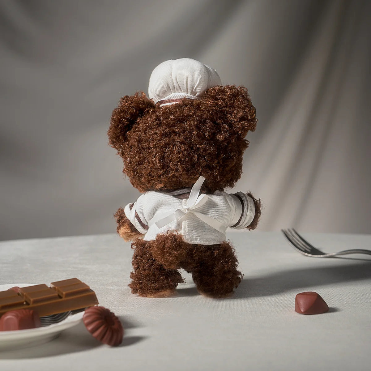 Back of LITTLE BUNS chef doll showing brown bear hood, toque and bow-tied chef apron, Melting Together series