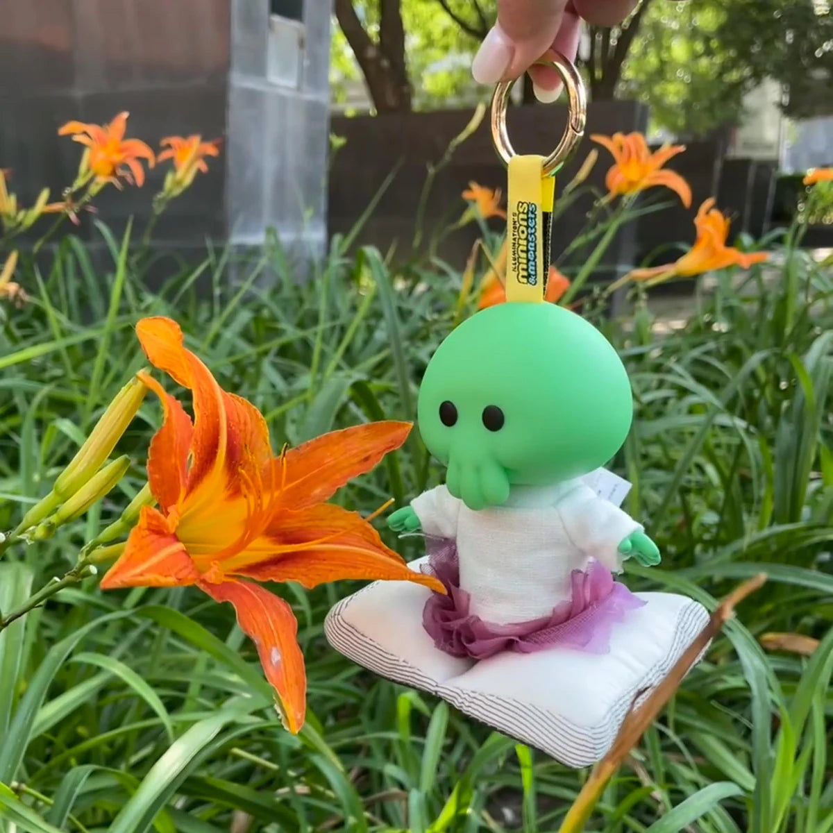 Goomi plush keychain hanging beside orange daylilies outdoors