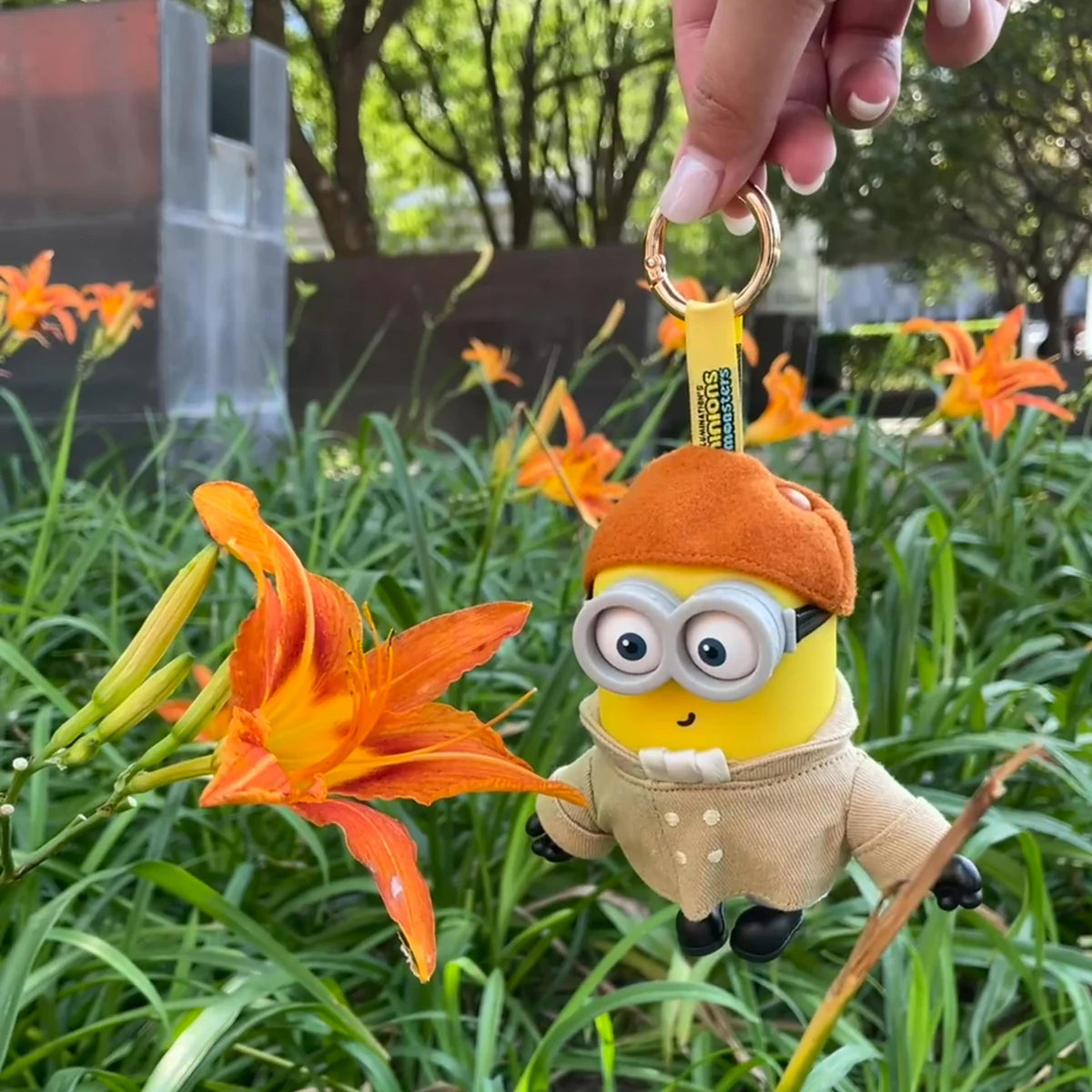 Artist Henry Minion plush keychain hanging beside orange daylilies