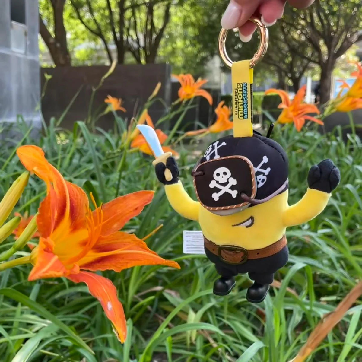 Pirate Carl Minion plush keychain hanging beside orange daylilies