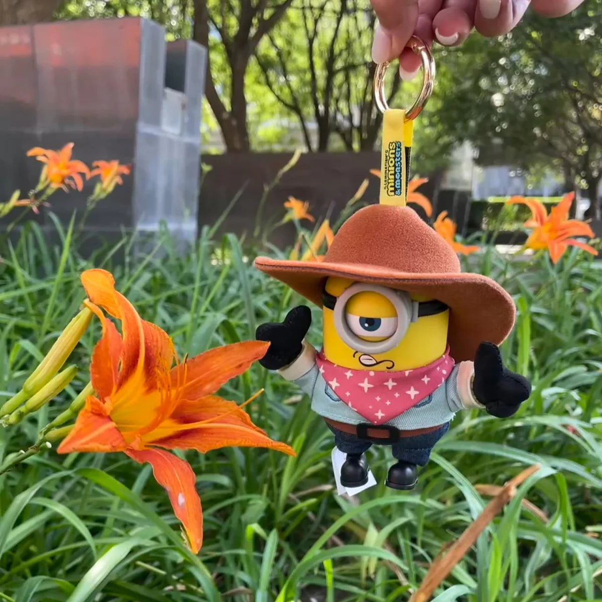 Cowboy James Minion plush keychain hanging beside orange daylilies