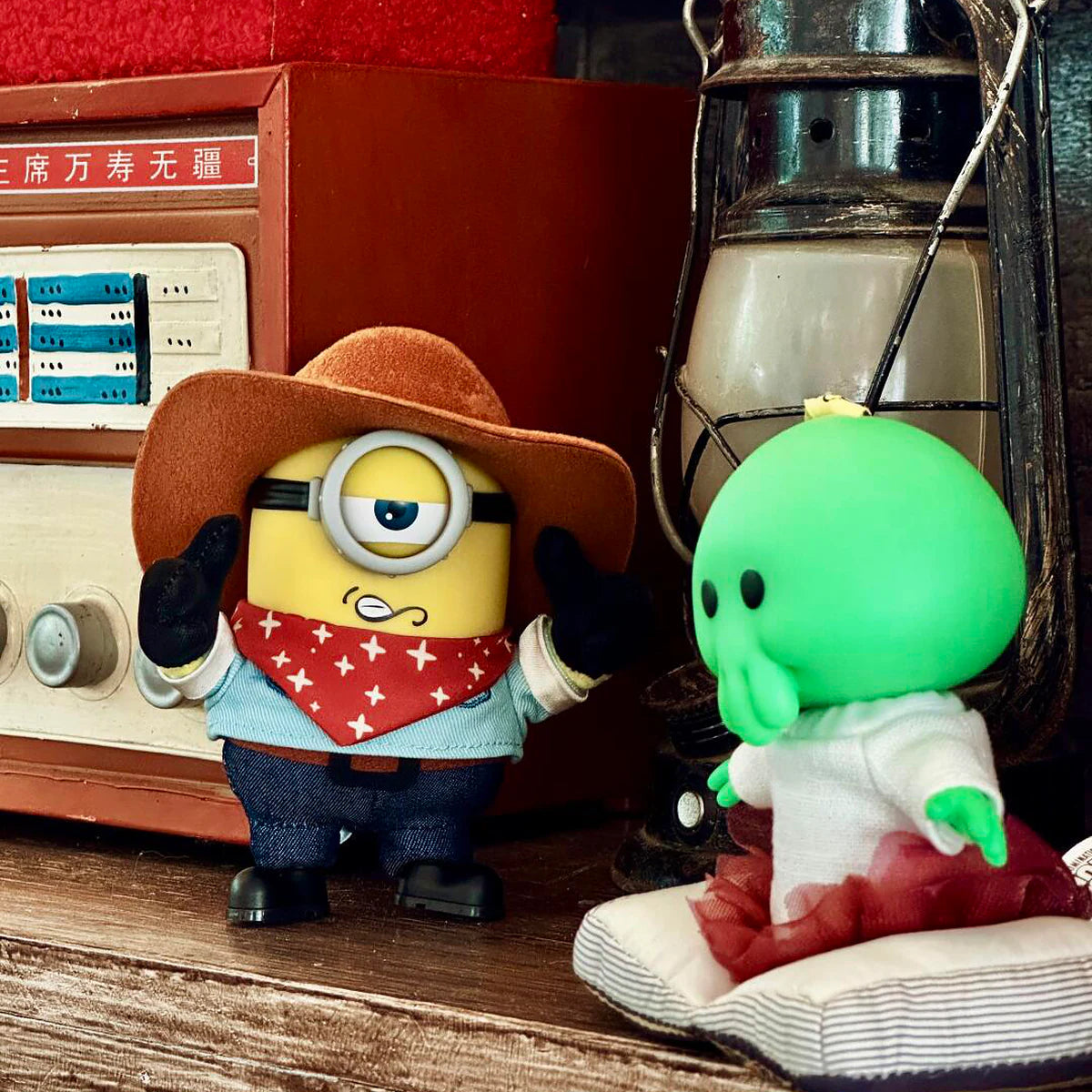 Cowboy James Minion plush facing Goomi beside a vintage radio and lantern