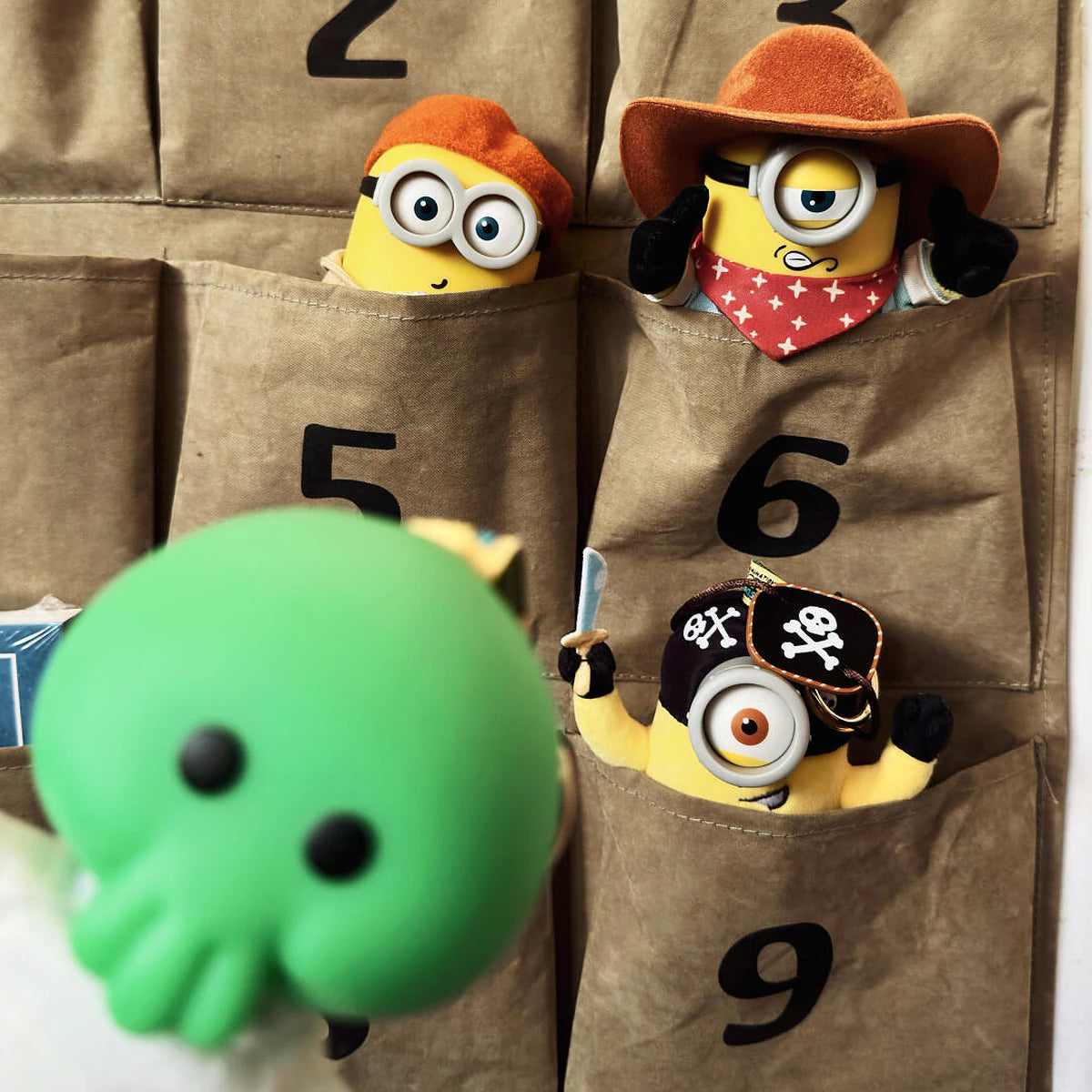 Goomi in front of numbered fabric pockets containing the three Minion plush designs