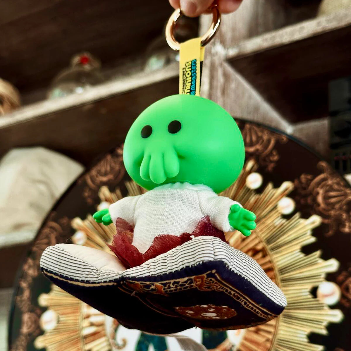 Goomi plush keychain suspended over a patterned cushion