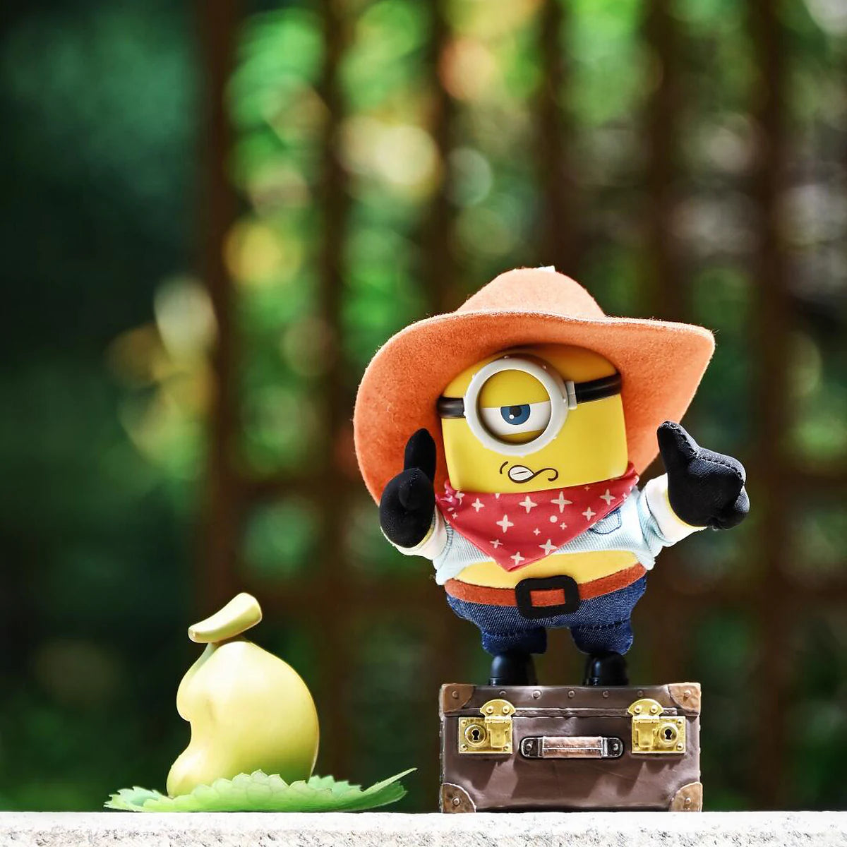 Cowboy James Minion plush standing on a suitcase beside a yellow money bag