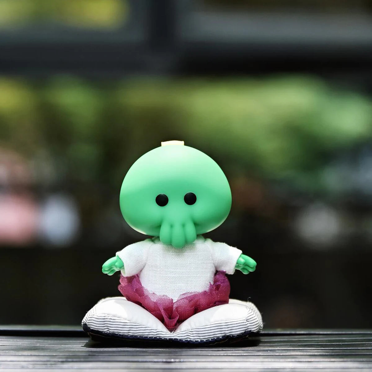 Goomi green monster plush seated alone on a wooden surface outdoors