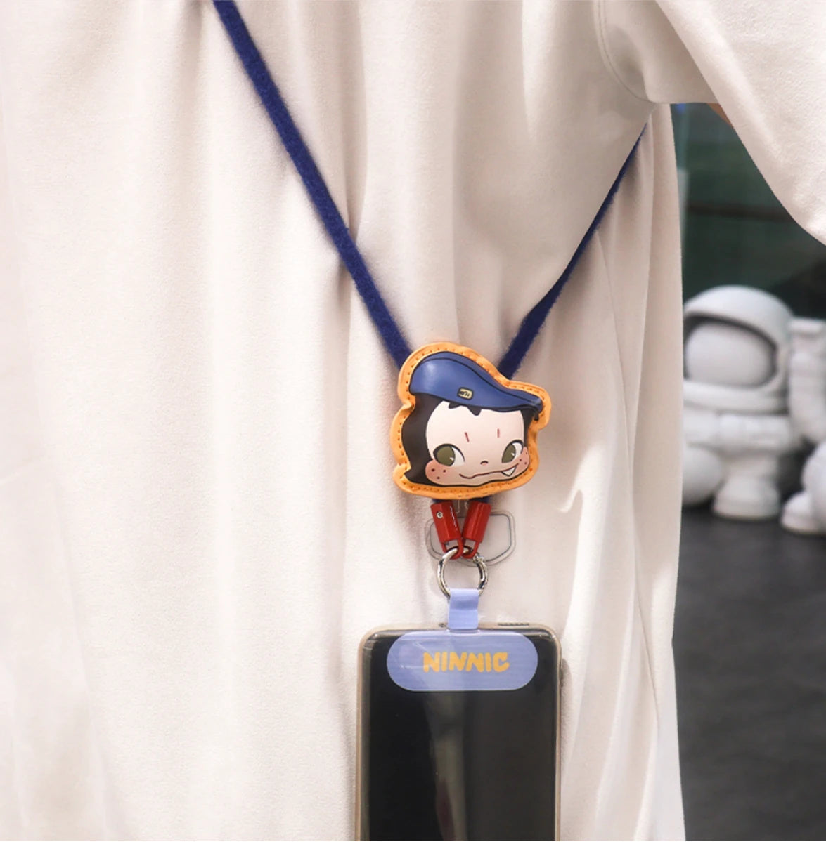 Coffee Watcher navy lanyard with blue-cap boy charm worn across the chest holding a phone, NINNIC Wild & Free