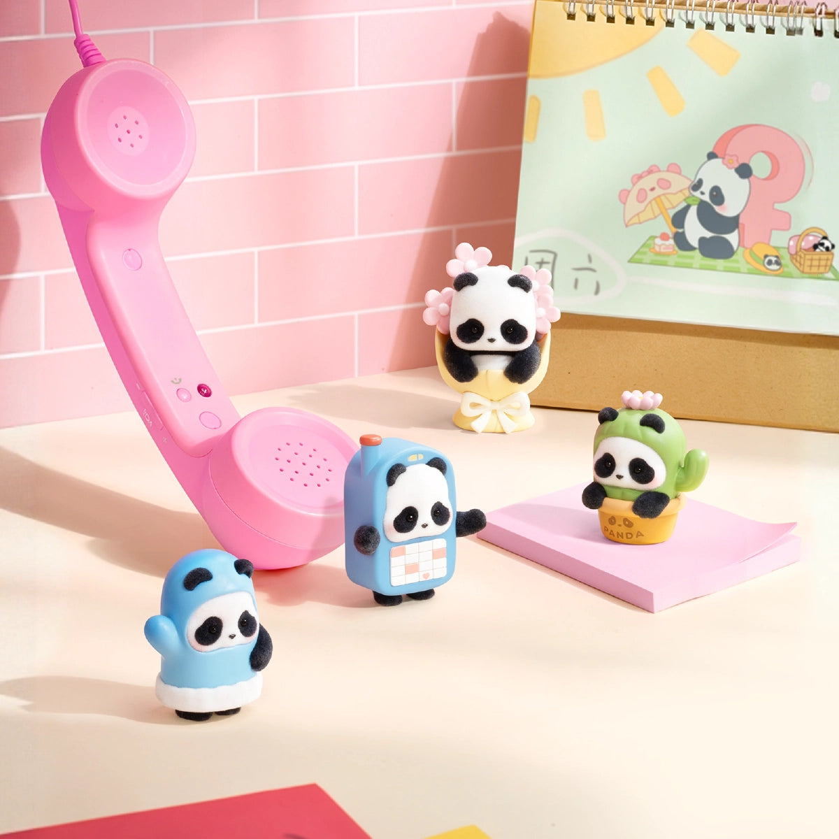 Four Panda Roll MiniMe figures displayed beside a pink telephone and notebook