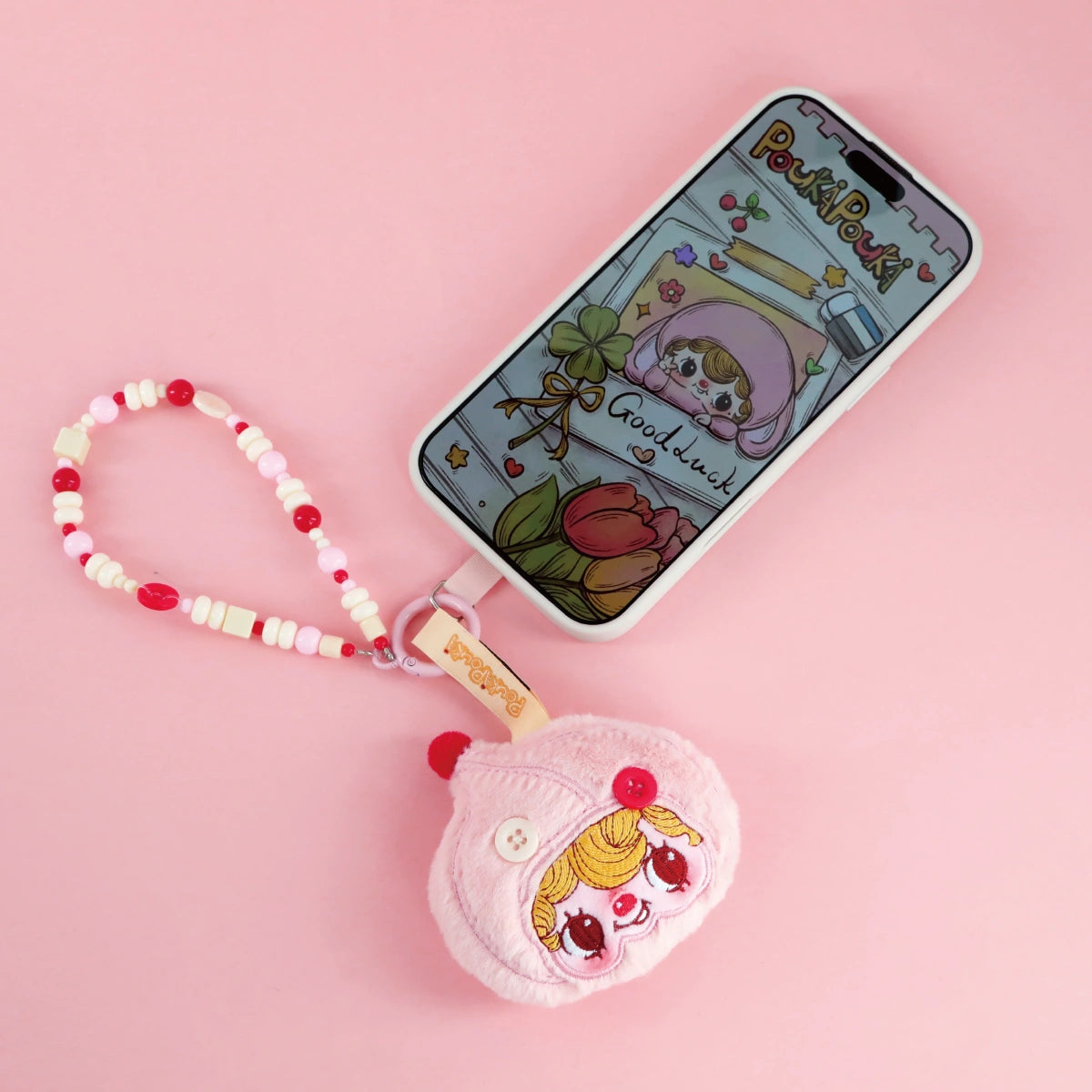 POUKA Childhood pink plush button phone charm clipped to a phone with matching wallpaper