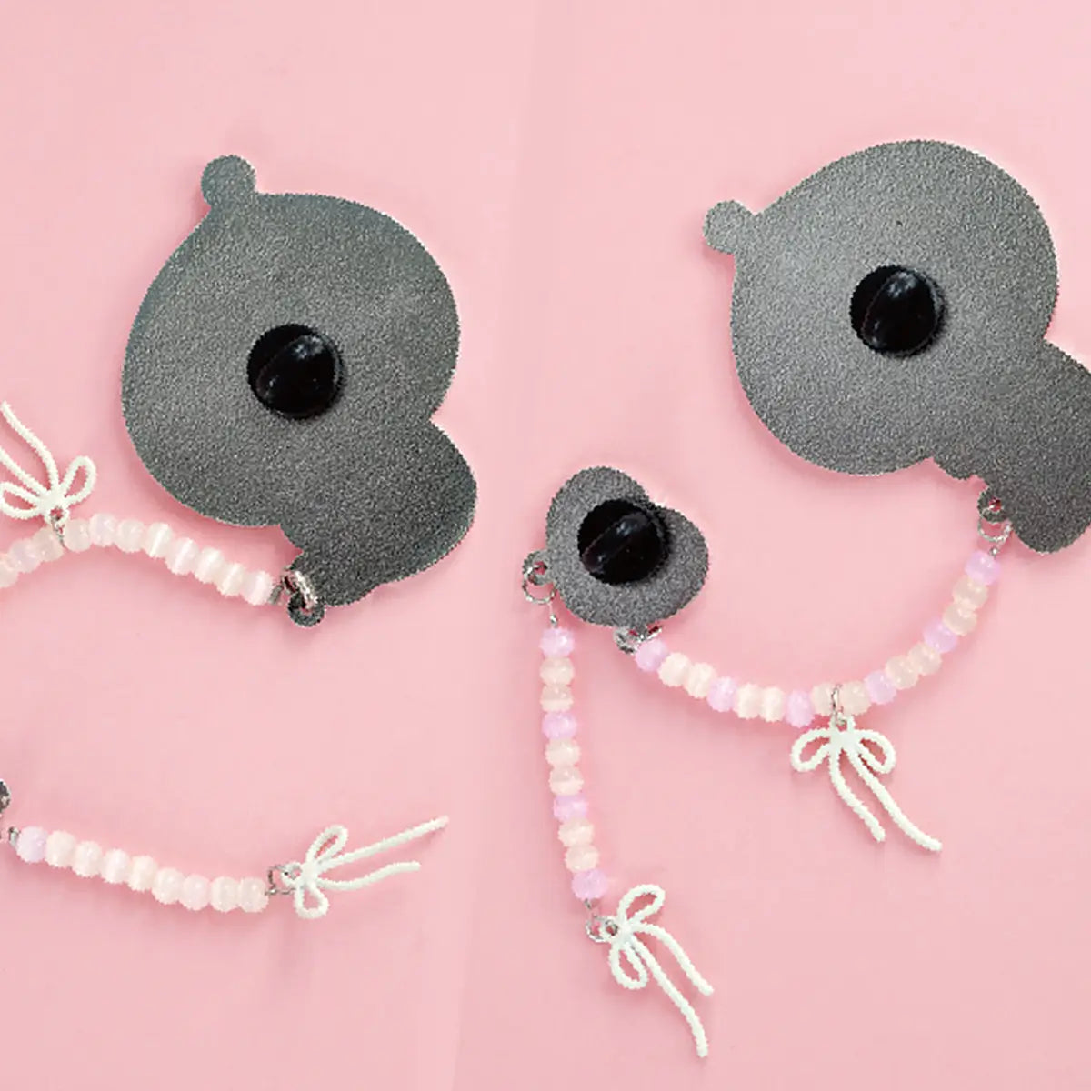 Back view of two POUKA enamel brooches showing pin clasps and beaded bow straps, POUKAPOUKA series