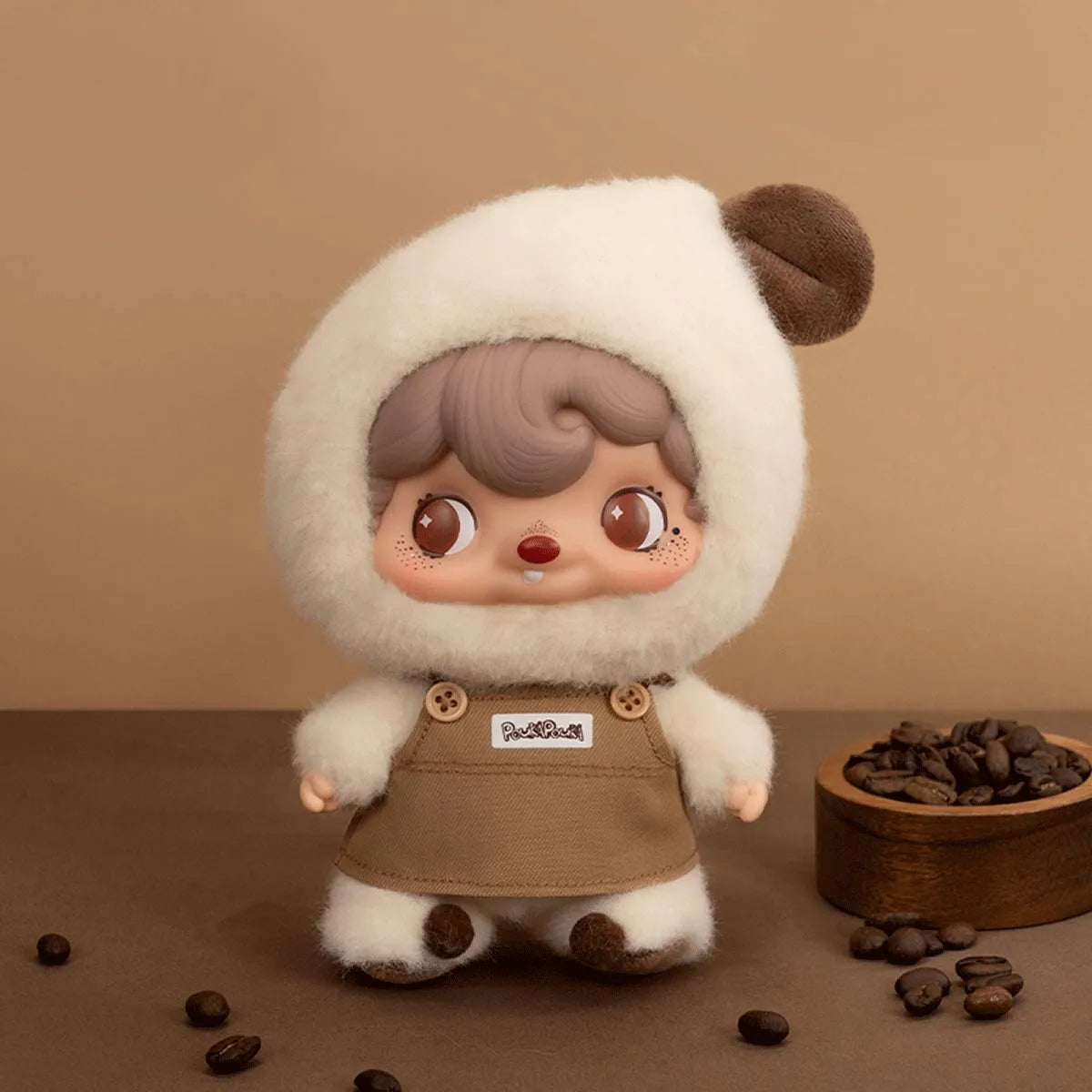 Pouka Pouka Coffee Time plush doll in milk-foam hood and tan apron beside a bowl of roasted coffee beans