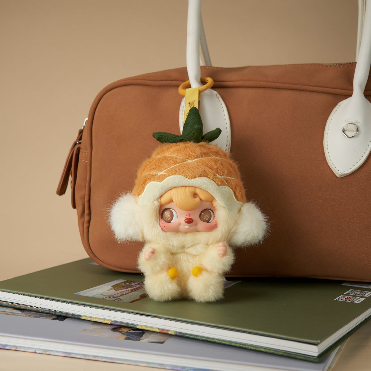POUKAPOUKA Mini Pineapple vinyl plush charm hanging from a brown handbag