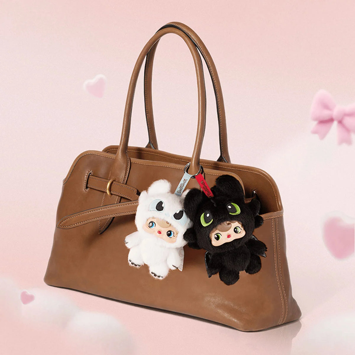 White and black POUKA dragon plush keychains clipped to a brown leather handbag
