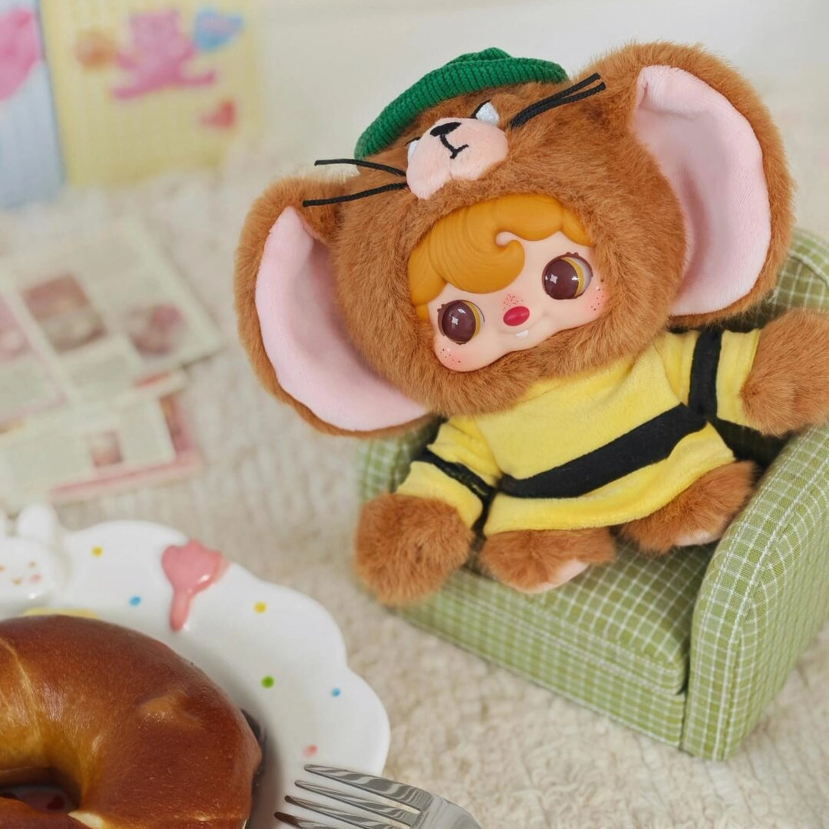 Secret POUKAPOUKA Jerry costume reclining in a tiny green chair beside a pastry