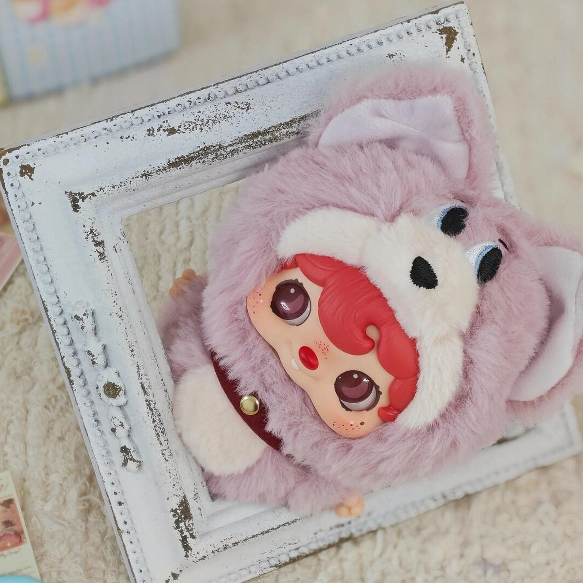 POUKAPOUKA in a lavender Tom costume with red hair lying inside a white frame