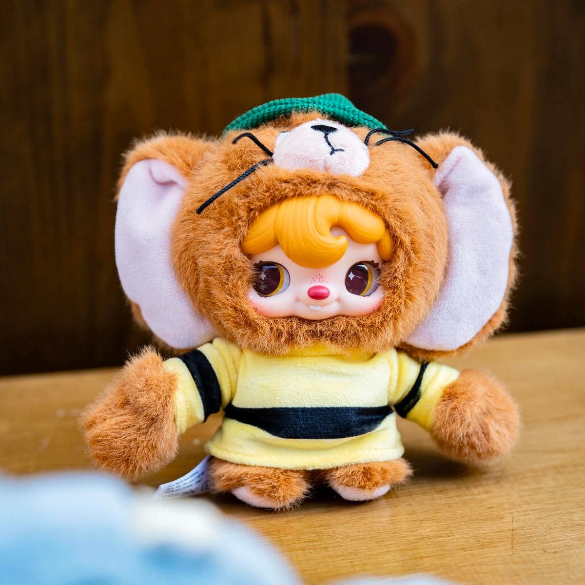 Secret POUKAPOUKA in a brown Jerry costume with striped shirt on a wooden table