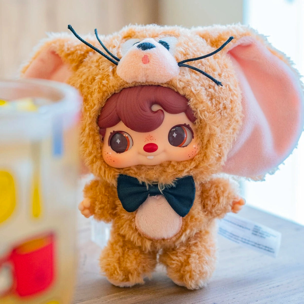 POUKAPOUKA in a brown Jerry costume with black bow tie standing on a desk