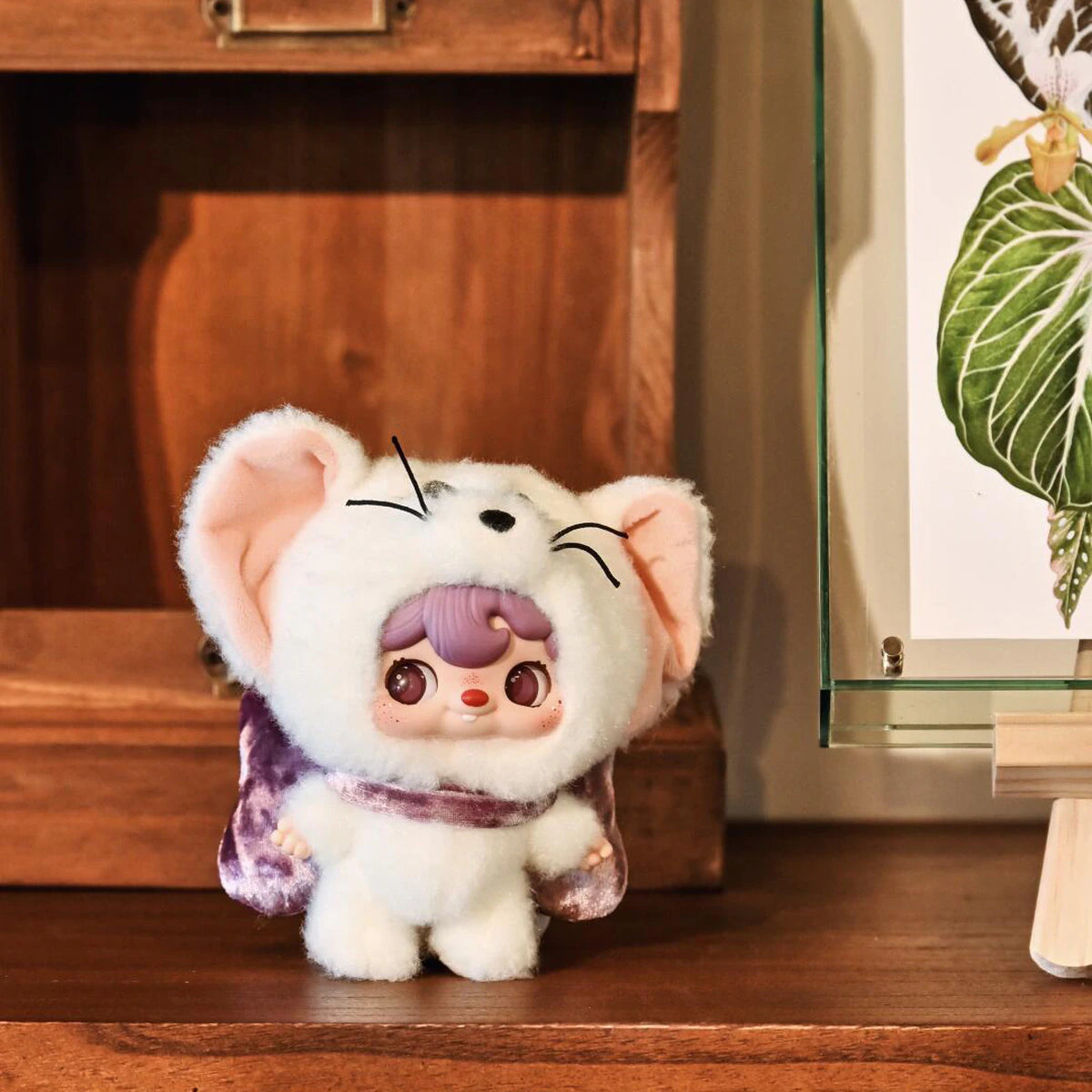 POUKAPOUKA in a white Tom costume with purple hair beside a wooden cabinet